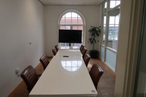 Vergaderruimte aan het Gedempt Hamerkanaal met lange witte tafel, leren stoelen, televisie en groot boograam.